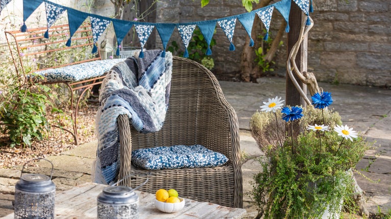 A garden chair with a throw, an outdoor cushion and bunting from the SS 2025 collection